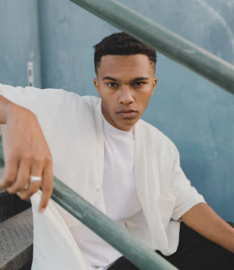 A person in a crisp white t-shirt leaning against a railing, photographed from a stylish angle with modern architectural elements in the background
